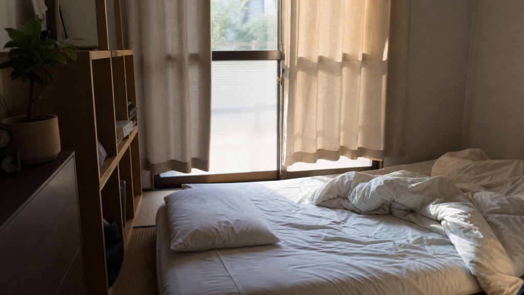 疲れを回復する朝の日本の部屋で、半分閉じたカーテンと少し乱れたベッドがある様子
